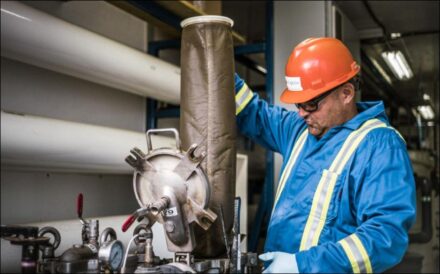 Man in hard hat, goggles and overalls working at machine.